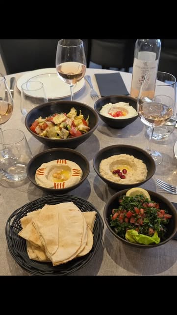 Table dressée avec houmous, taboulé, pain pita et vin, prête à partager